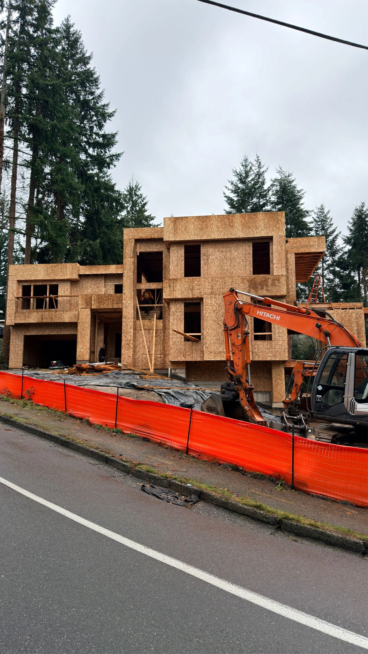 Modern house framing site with an orange excavator awaiting the installation of premium Luxury home windows.